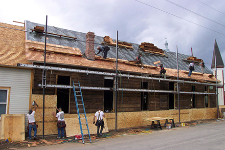 Workers replacing the roof and beginning work on the siding.